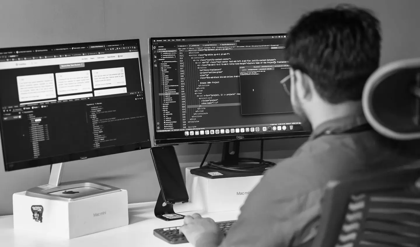 A developer writing code at two monitors